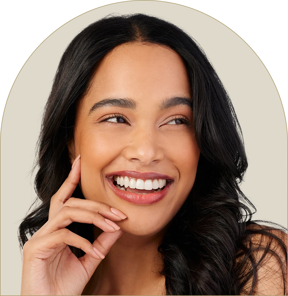 Young woman with dark wavy hair smiling broadly, hand near face