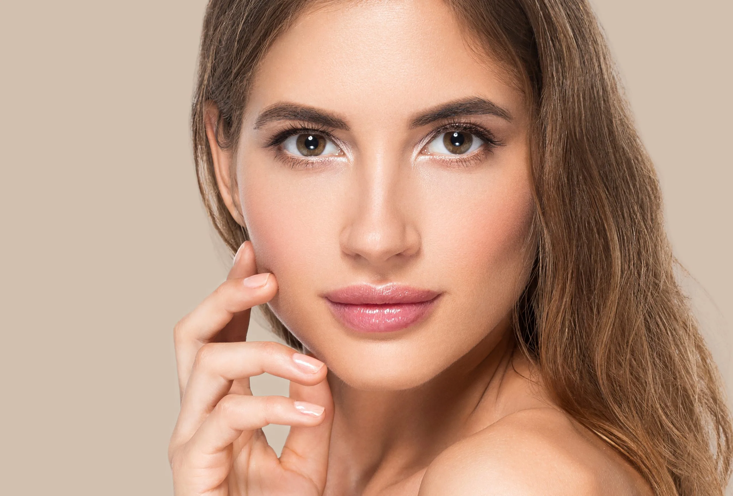 Woman with brown hair touching her face, looking at camera with clear skin