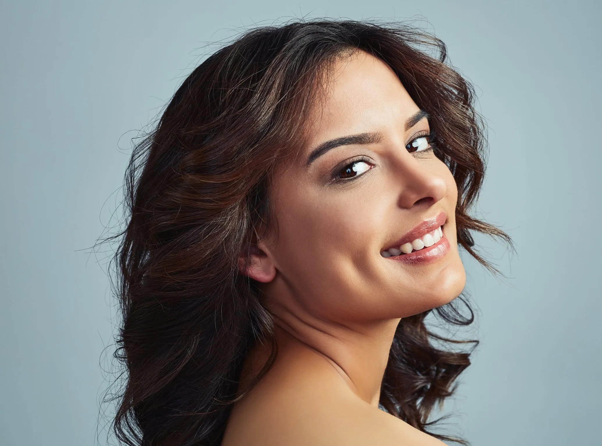 Woman with wavy dark hair smiling, looking over shoulder
