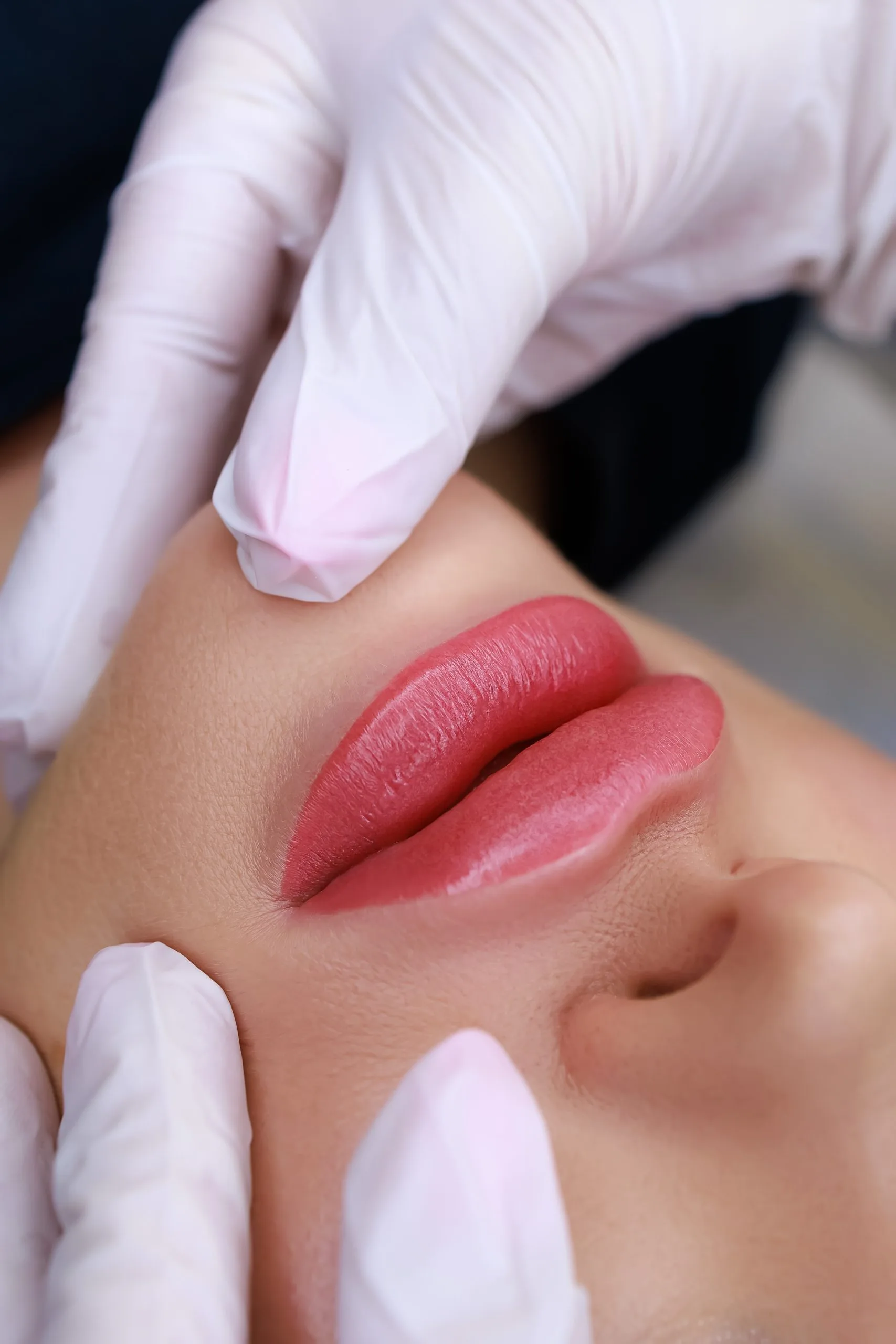 Practitioner in white gloves applying cosmetic treatment to woman's lips showing red-toned result