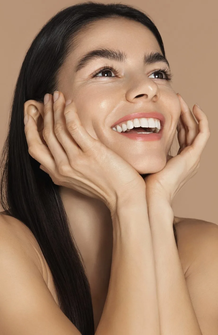 Woman with hands framing face, displaying bright smile and clear complexion
