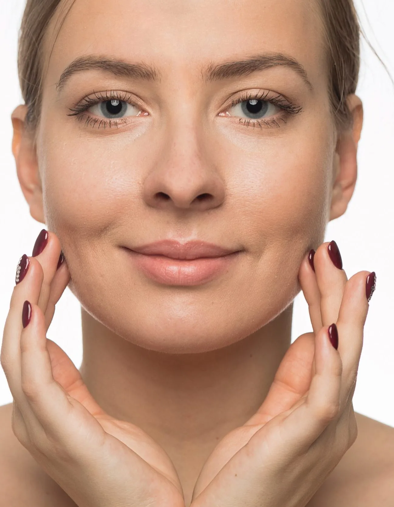 Woman with hands framing face, touching cheeks, with clear skin and burgundy manicure