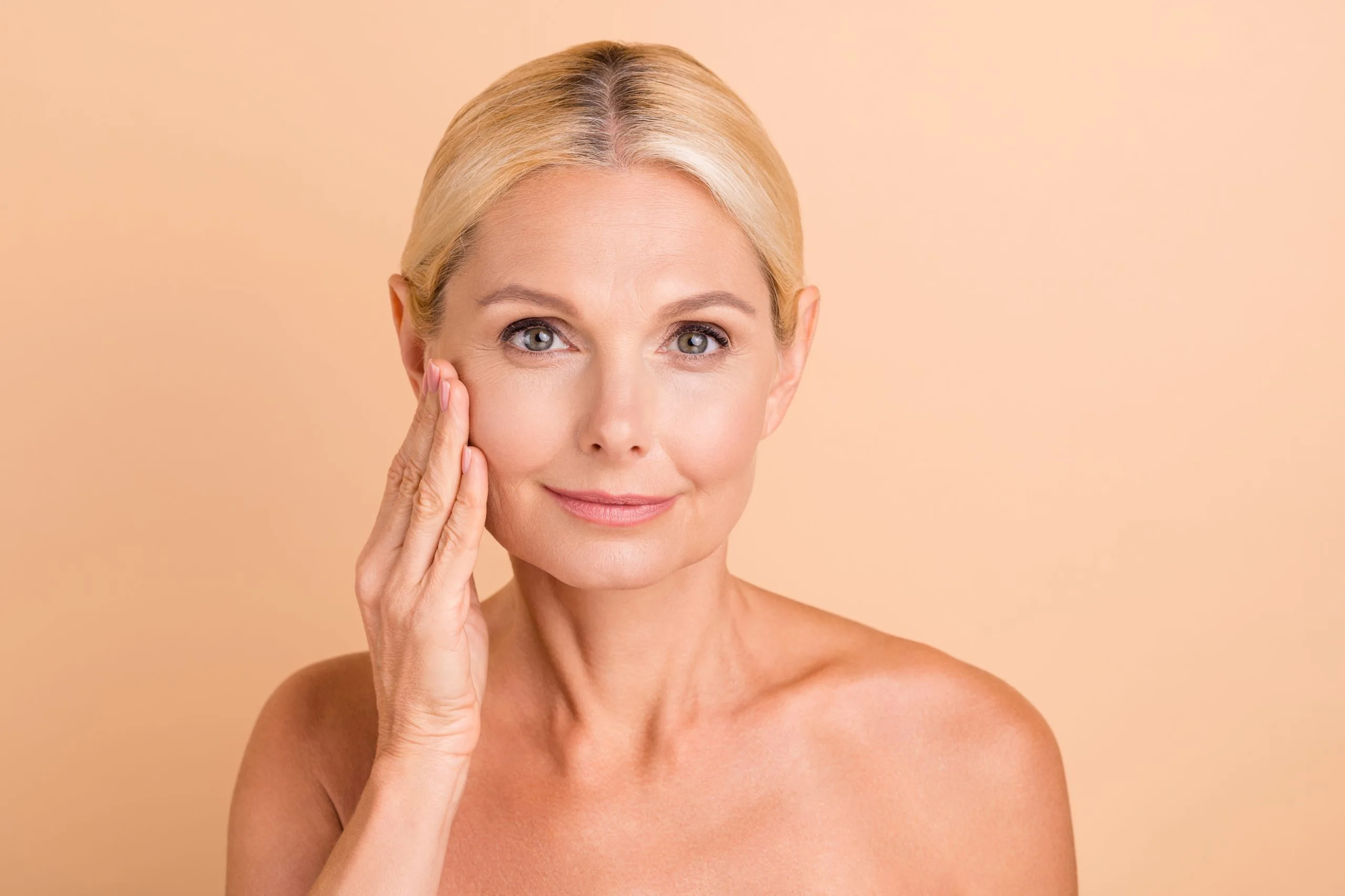 Woman touching her cheek and smiling against peach background