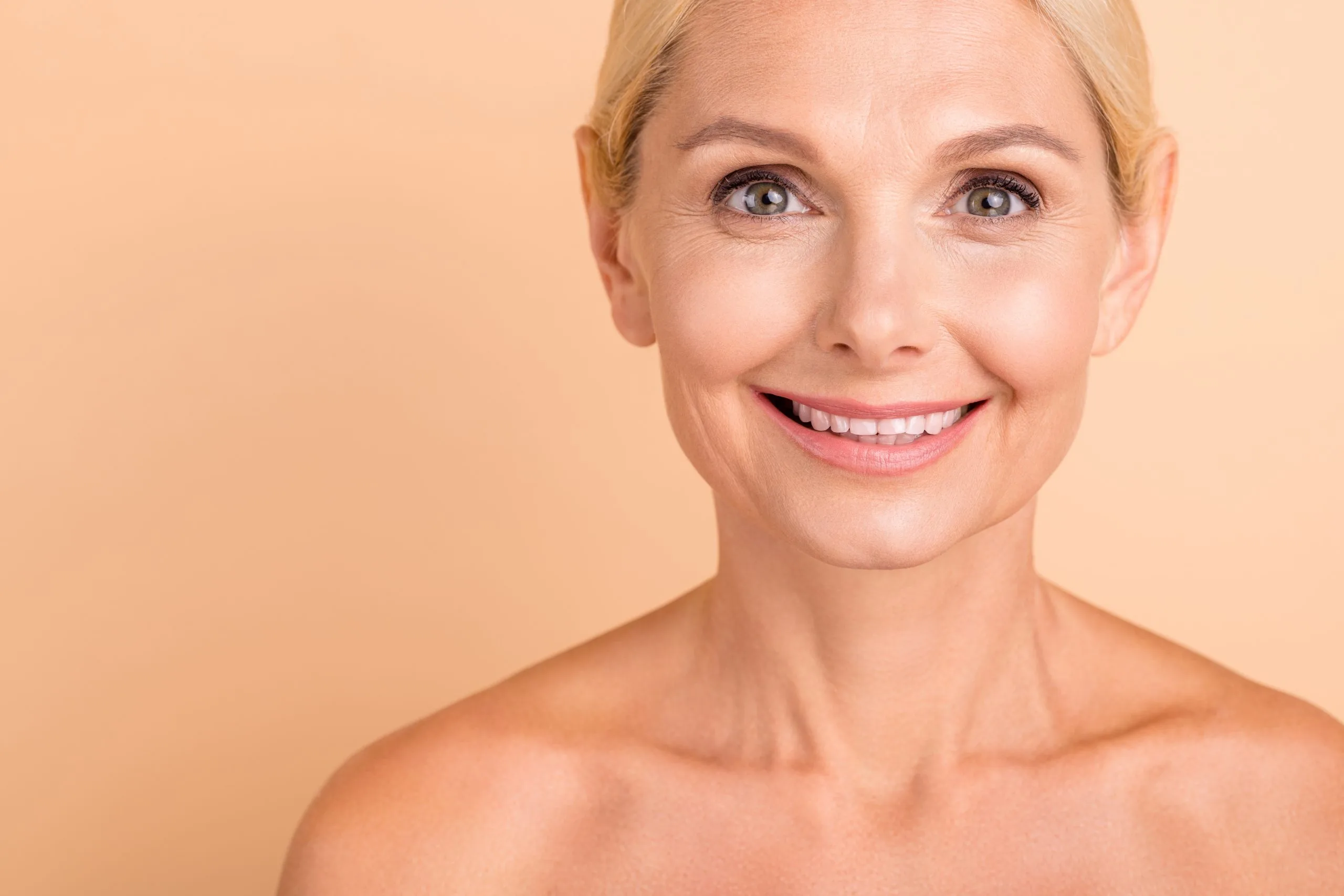 Blonde woman smiling at camera against tan background
