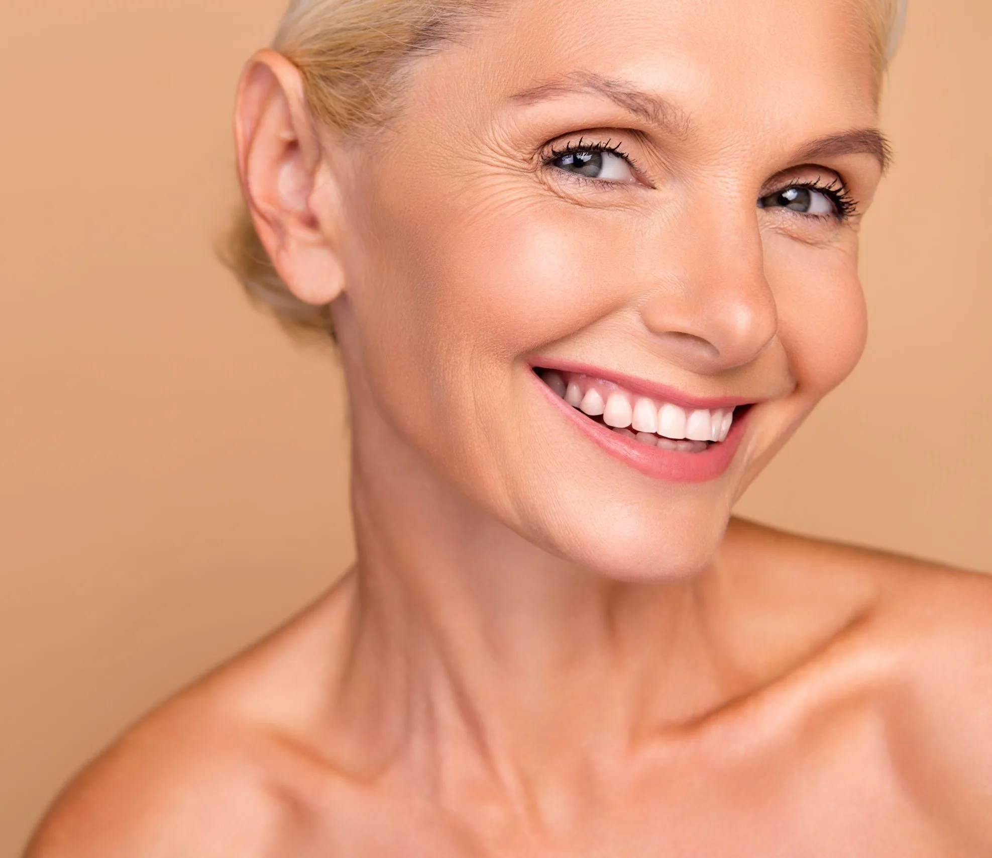Blonde woman smiling in three-quarter view against tan background