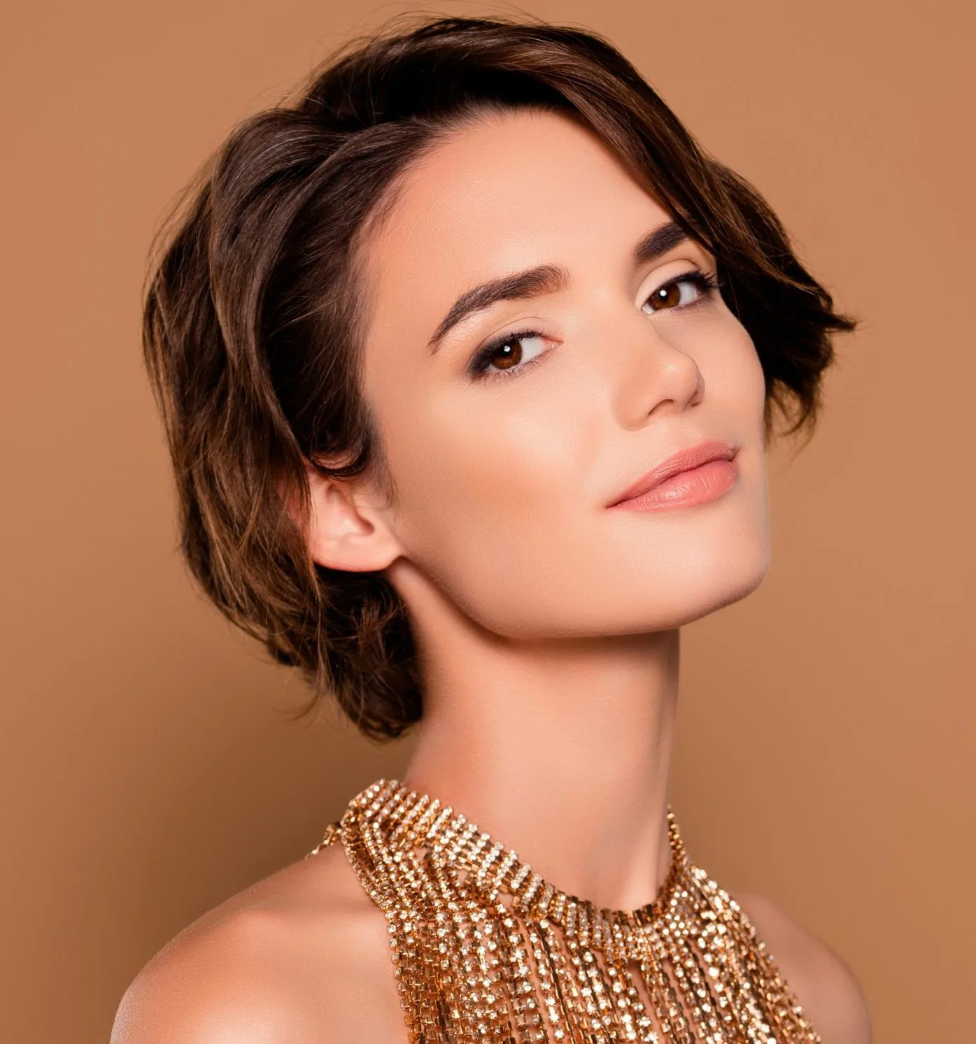 Woman with short wavy dark hair in profile against tan background wearing beaded garment