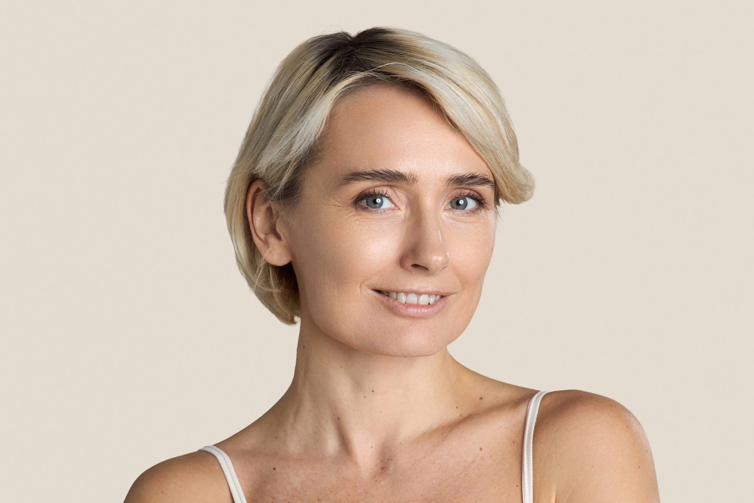 Woman with blonde bob haircut smiling at camera against neutral background