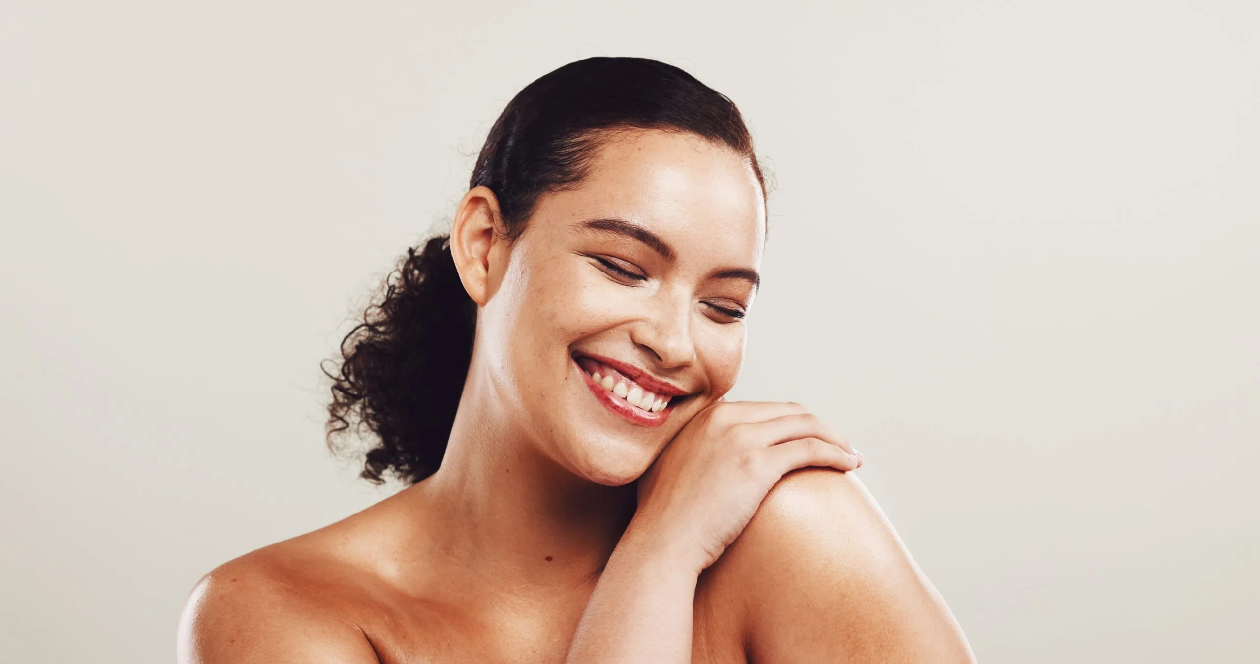Woman with curly dark hair smiling with hand near shoulder against a neutral background