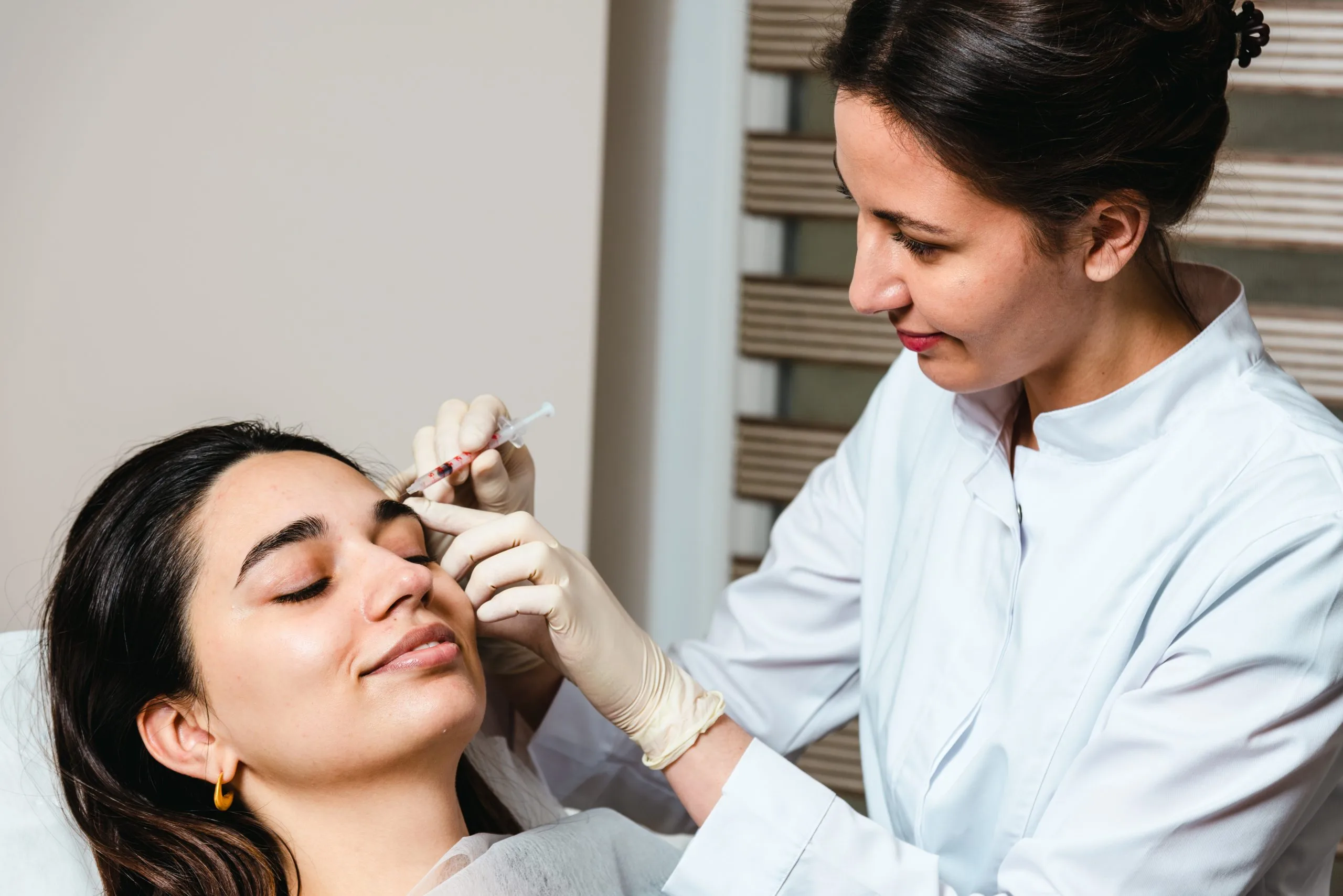 Practitioner injecting filler into patient's cheek during consultation