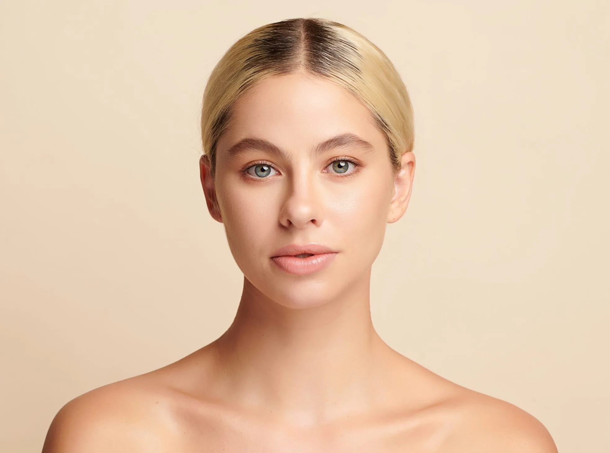 Woman with blonde hair facing camera with neutral expression against beige background