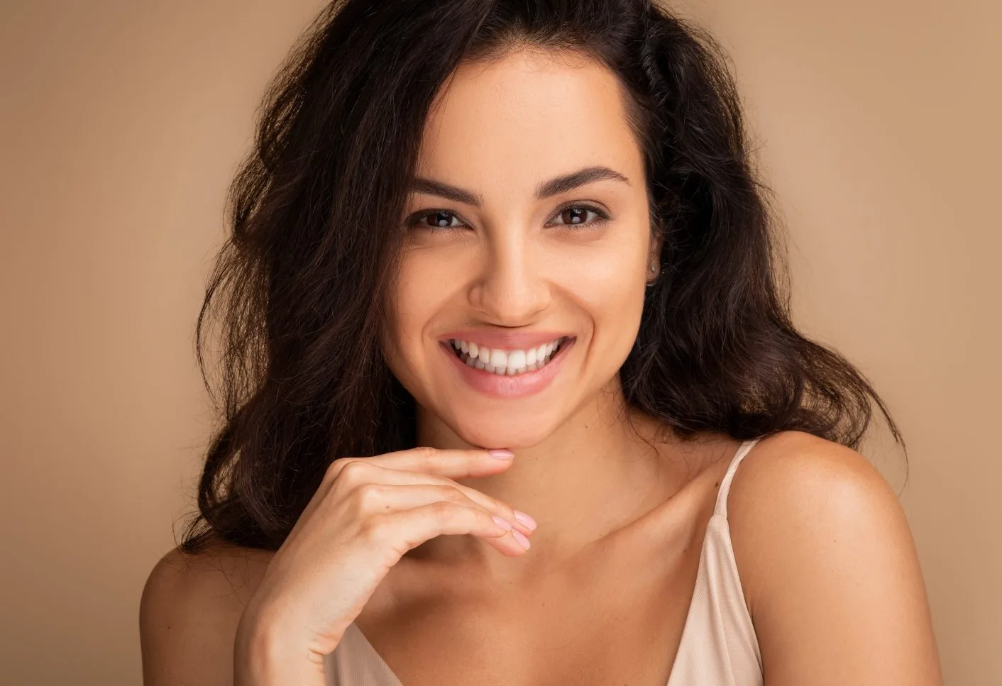 Woman with long dark hair smiling at camera against neutral background
