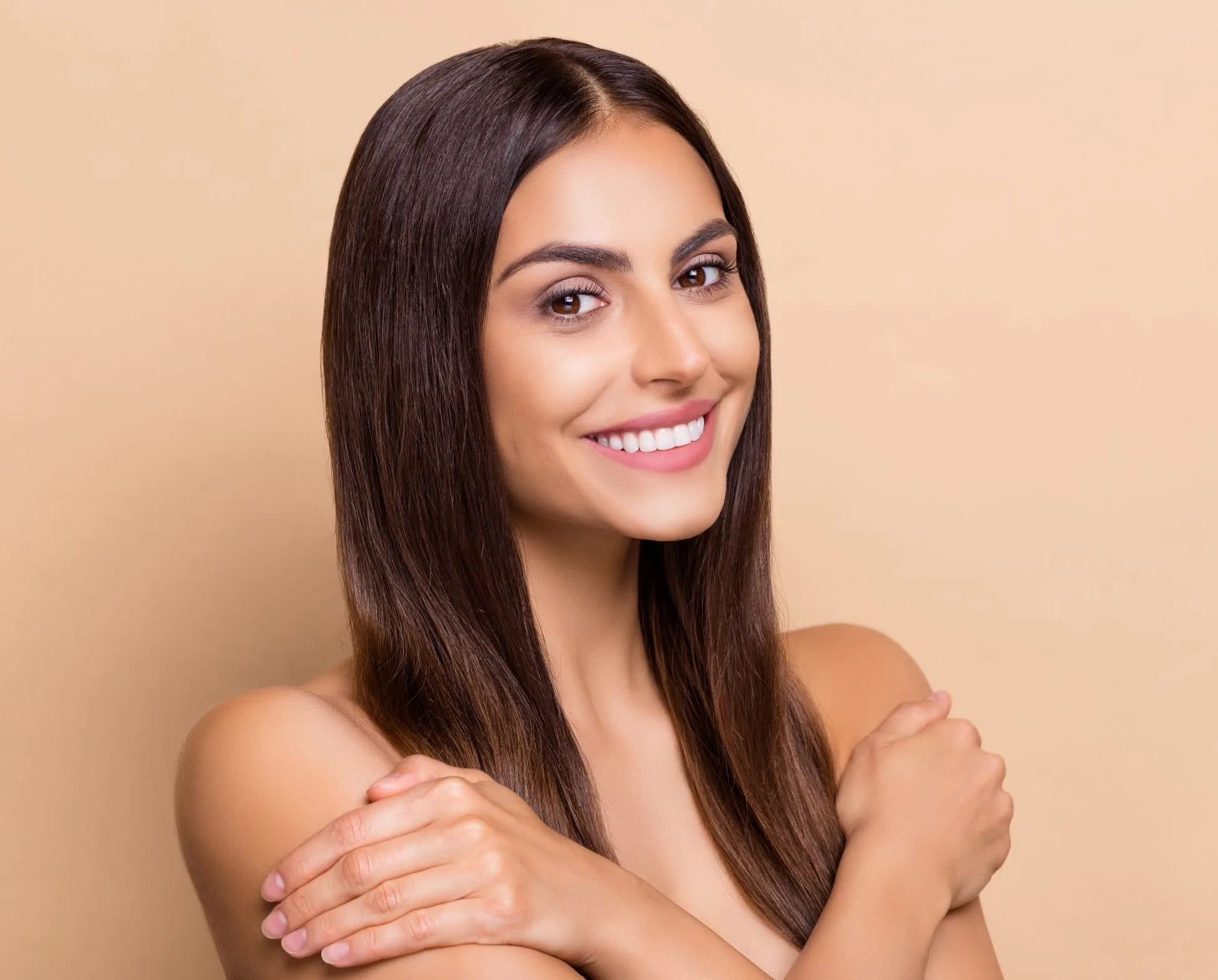 Smiling woman with long dark hair hugging her shoulders against a neutral background