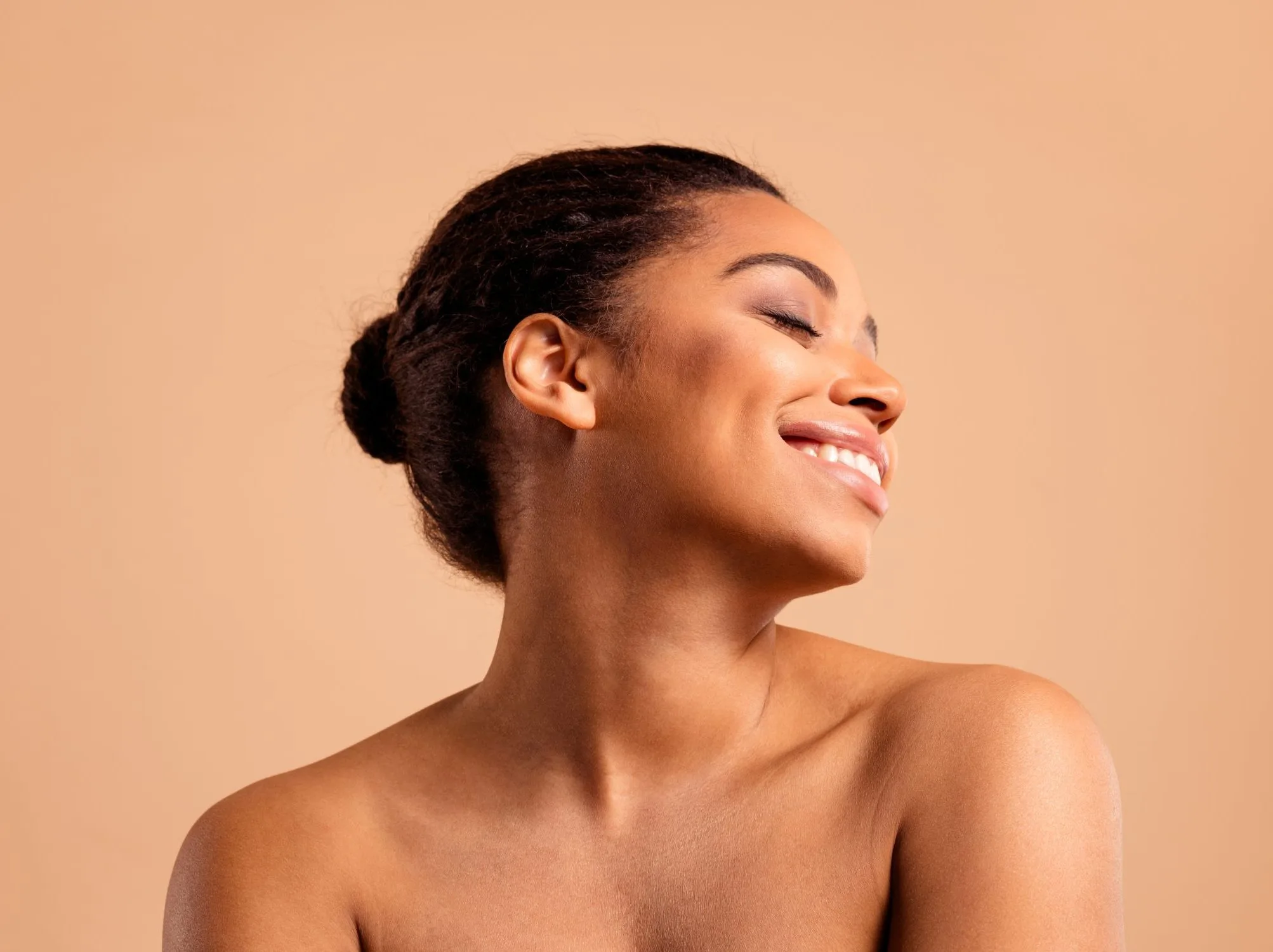 Woman with glowing skin smiling in profile against a beige background