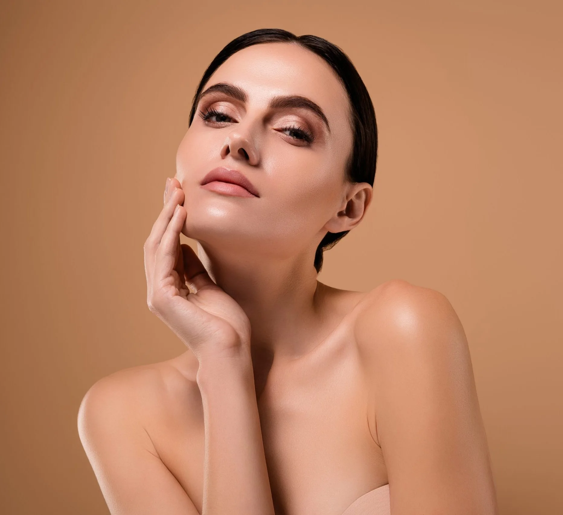 Woman touching her face, displaying clear, glowing skin against a neutral background