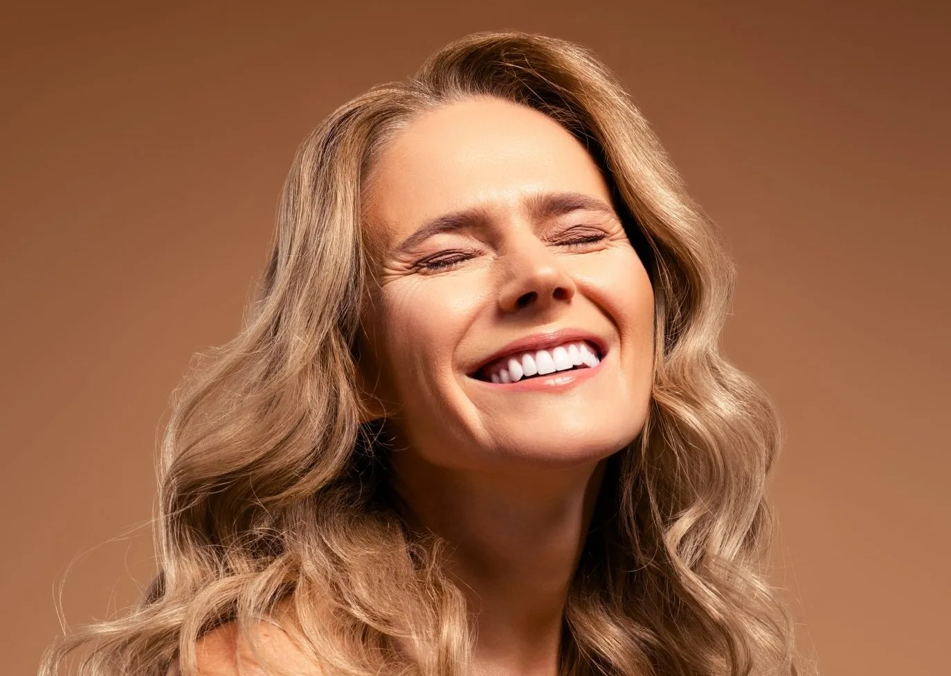 Mature woman smiling with eyes closed against warm brown background