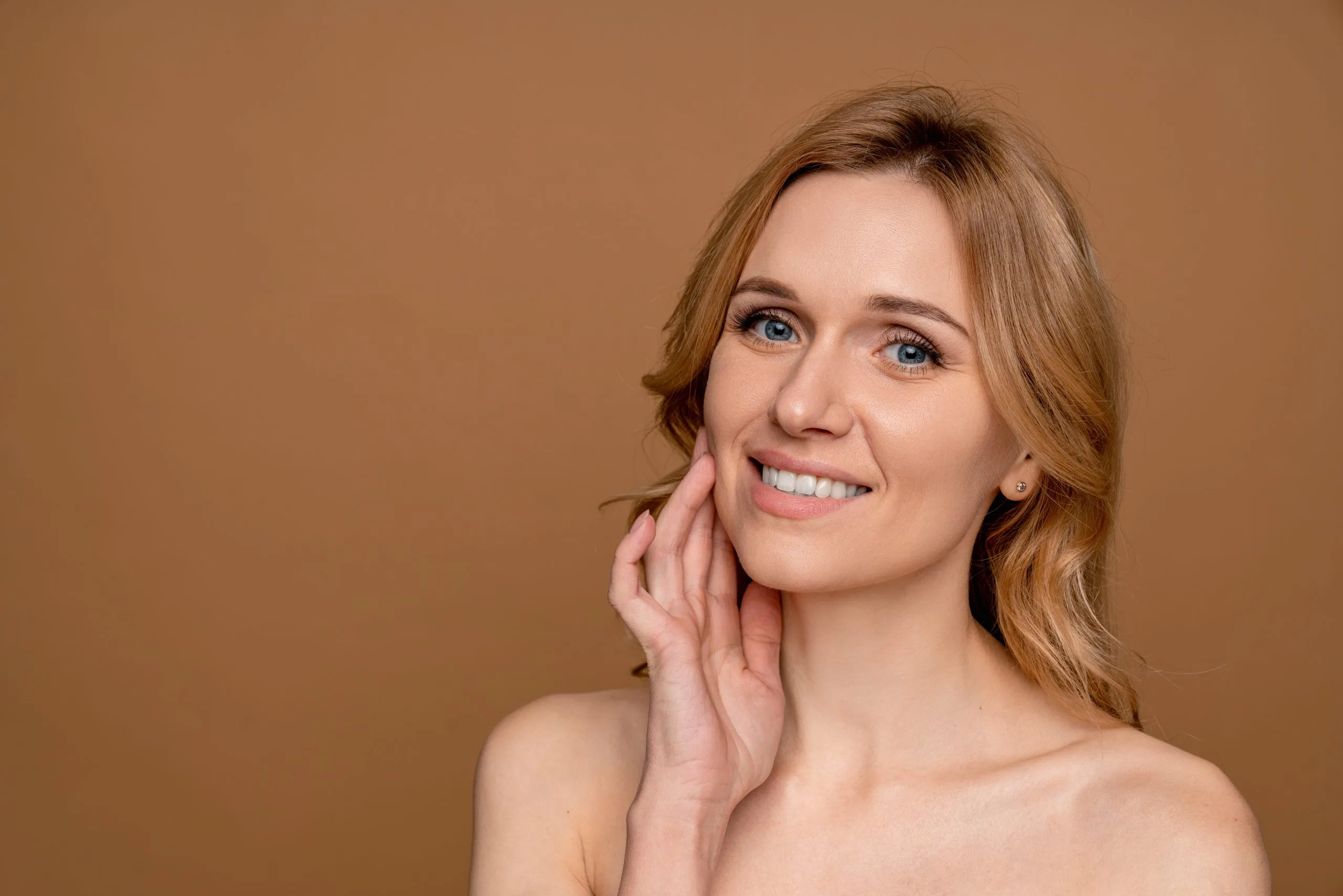 Woman with auburn hair touching her cheek, smiling at camera