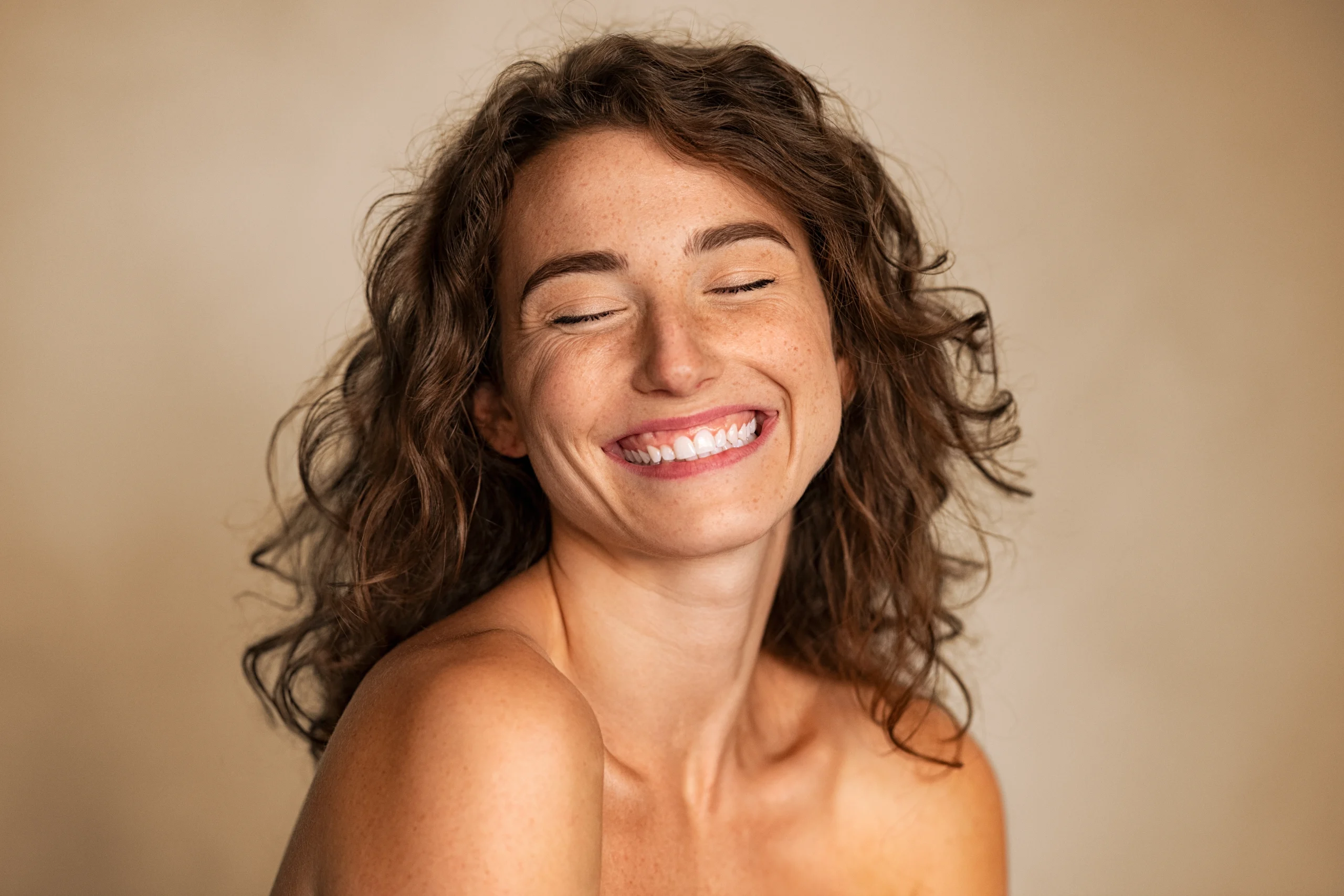 Joyful woman in her mid-thirties with curly hair, smiling against a warm background