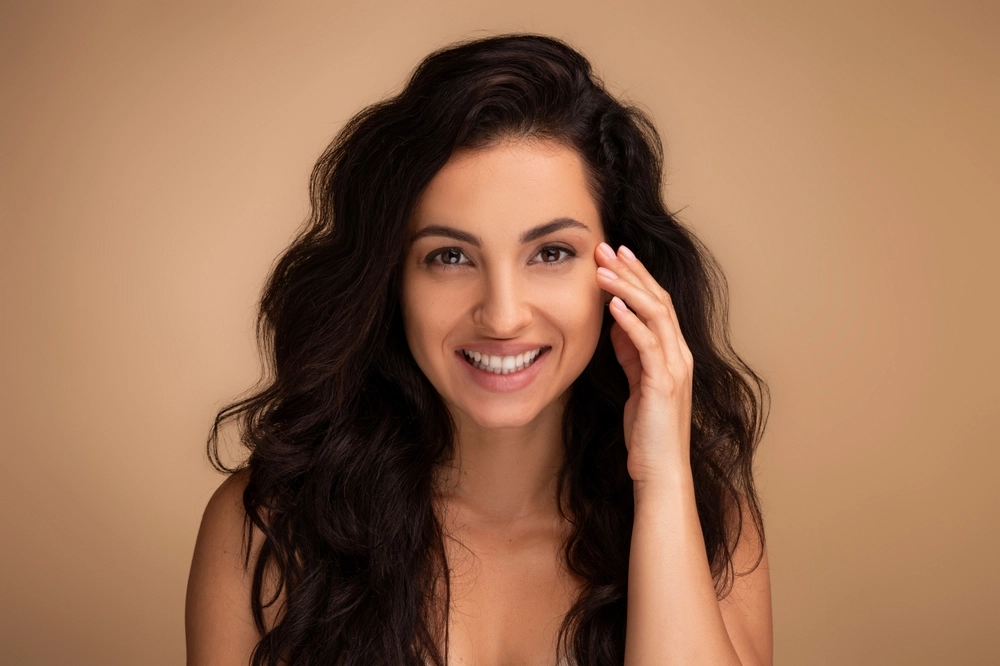 Smiling woman with wavy dark hair on a warm beige backdrop