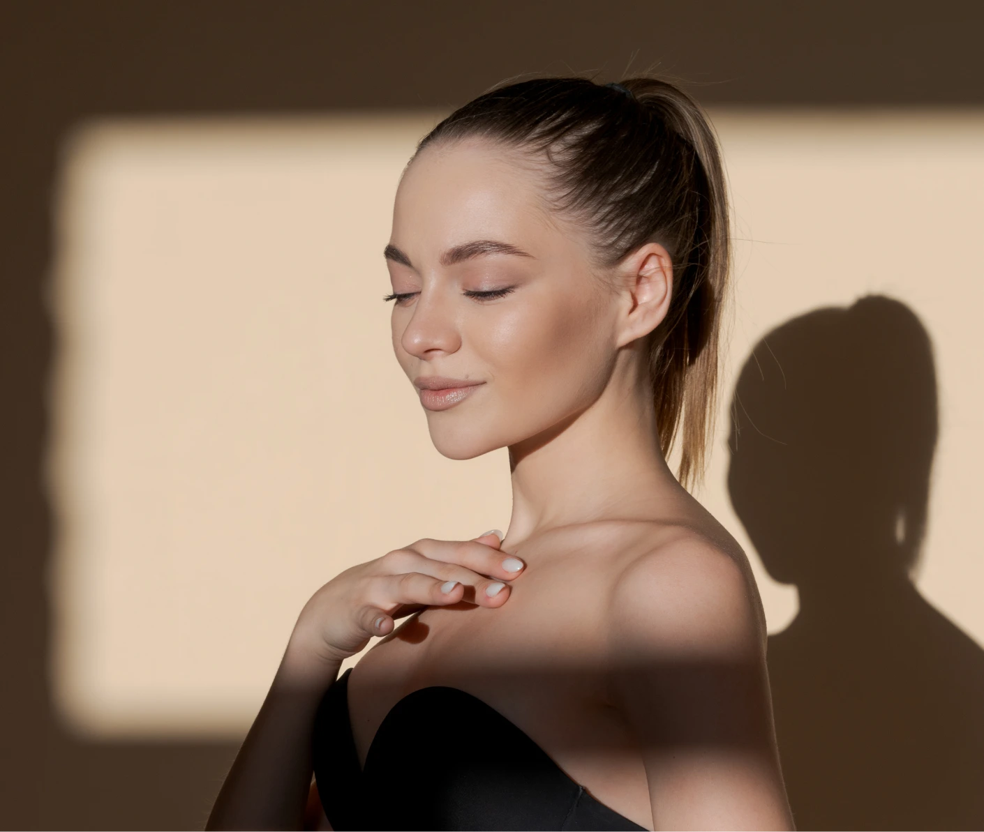 Woman in warm window light touching her collarbone